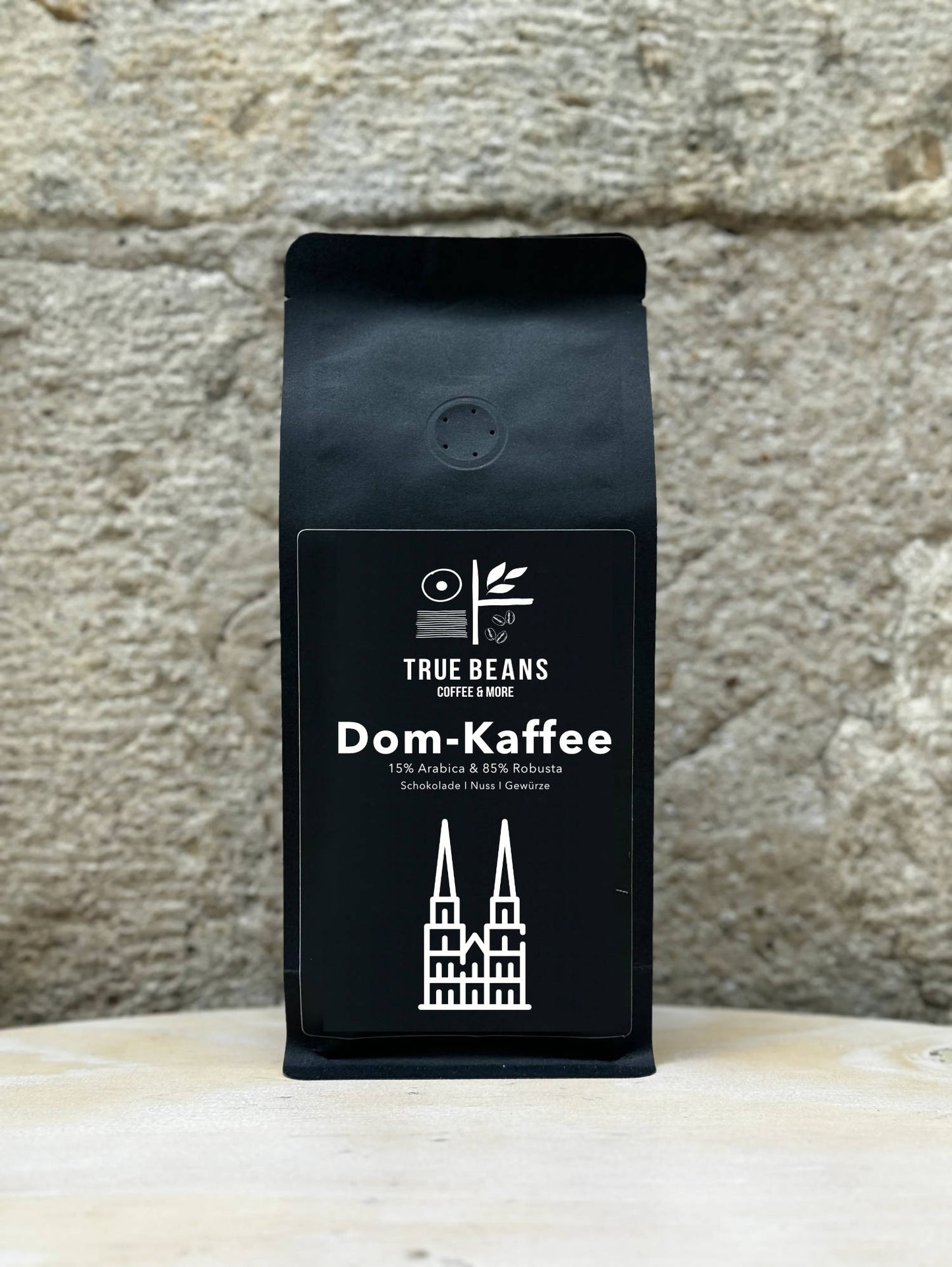 Ein Bild des Produkts Dom Kaffee von True Beans auf einem Holztisch vor einer steinernen Säule.