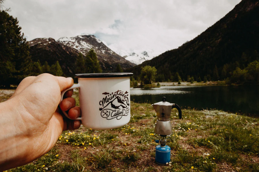Ein Becher Mokka Kaffee im Freien mit Bergblick und einer Espressokanne auf einem Campingkocher.