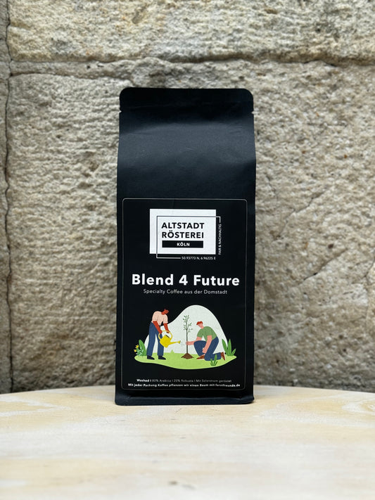 Eine Packung Altstadt Rösterei Köln Blend 4 Future Kaffee vor einer Steinwand. Auf der Verpackung ist eine Illustration von zwei Personen, die einen Baum pflanzen, sowie die Beschreibung "Specialty Coffee aus der Domstadt" zu sehen.