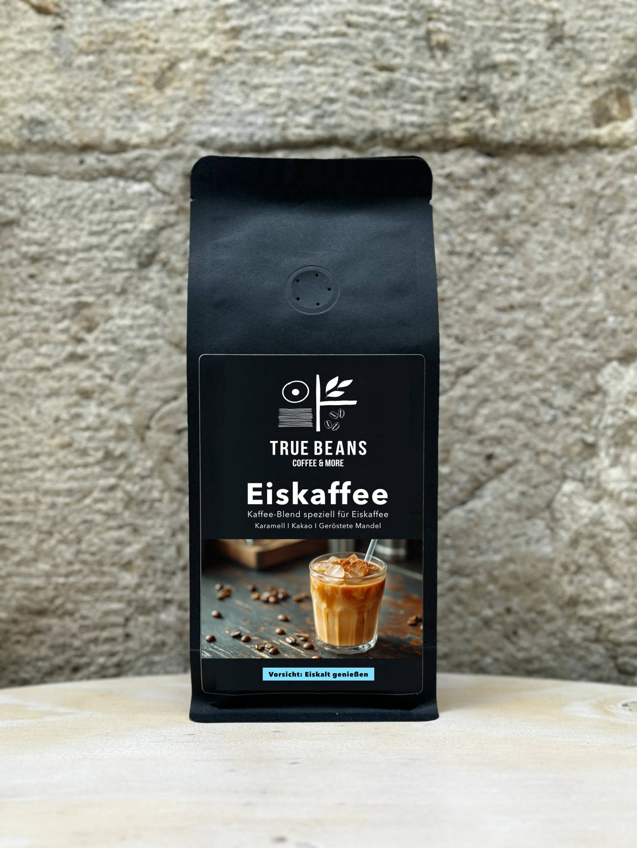 Ein Bild des Produkts Eiskaffe Blend von True Beans auf einem Holztisch vor einer steinernen Säule.
