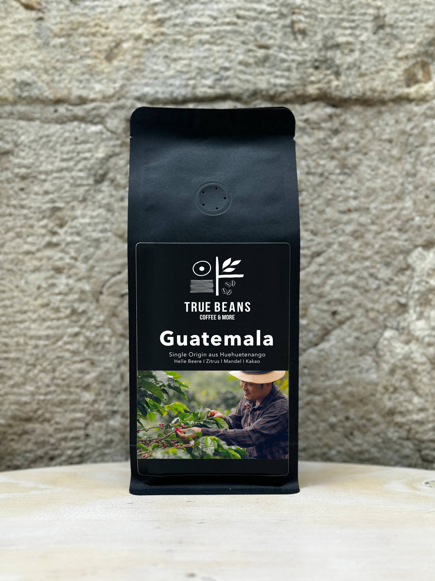 Ein Bild des Produkts Guatemala 100% Arabica von True Beans auf einem Holztisch vor einer steinernen Säule.