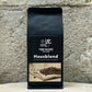 Ein Bild des Produkts Hausblend von True Beans auf einem Holztisch vor einer steinernen Säule.
