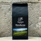 Ein Bild des Produkts 100% Honduras Arabica von True Beans auf einem Holztisch vor einer steinernen Säule.