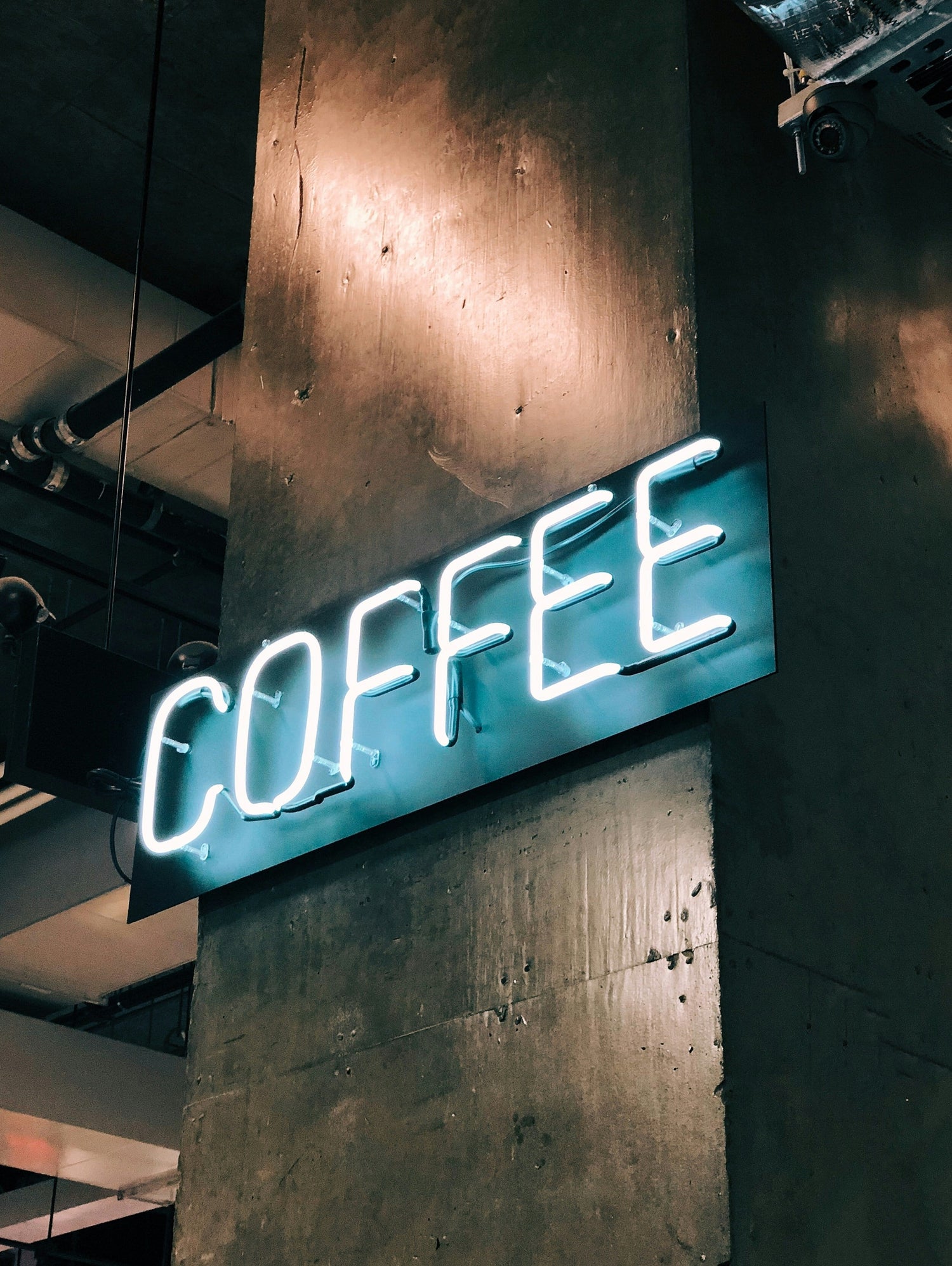 Ein leuchtendes Neon-Schild mit der Aufschrift "COFFEE" an einer Betonwand in einem industriellen Raum.