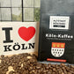  Eine Packung Köln-Kaffee von der Altstadt Rösterei Köln, umgeben von Kaffeebohnen. Daneben steht ein Schild mit der Aufschrift "I love Köln".