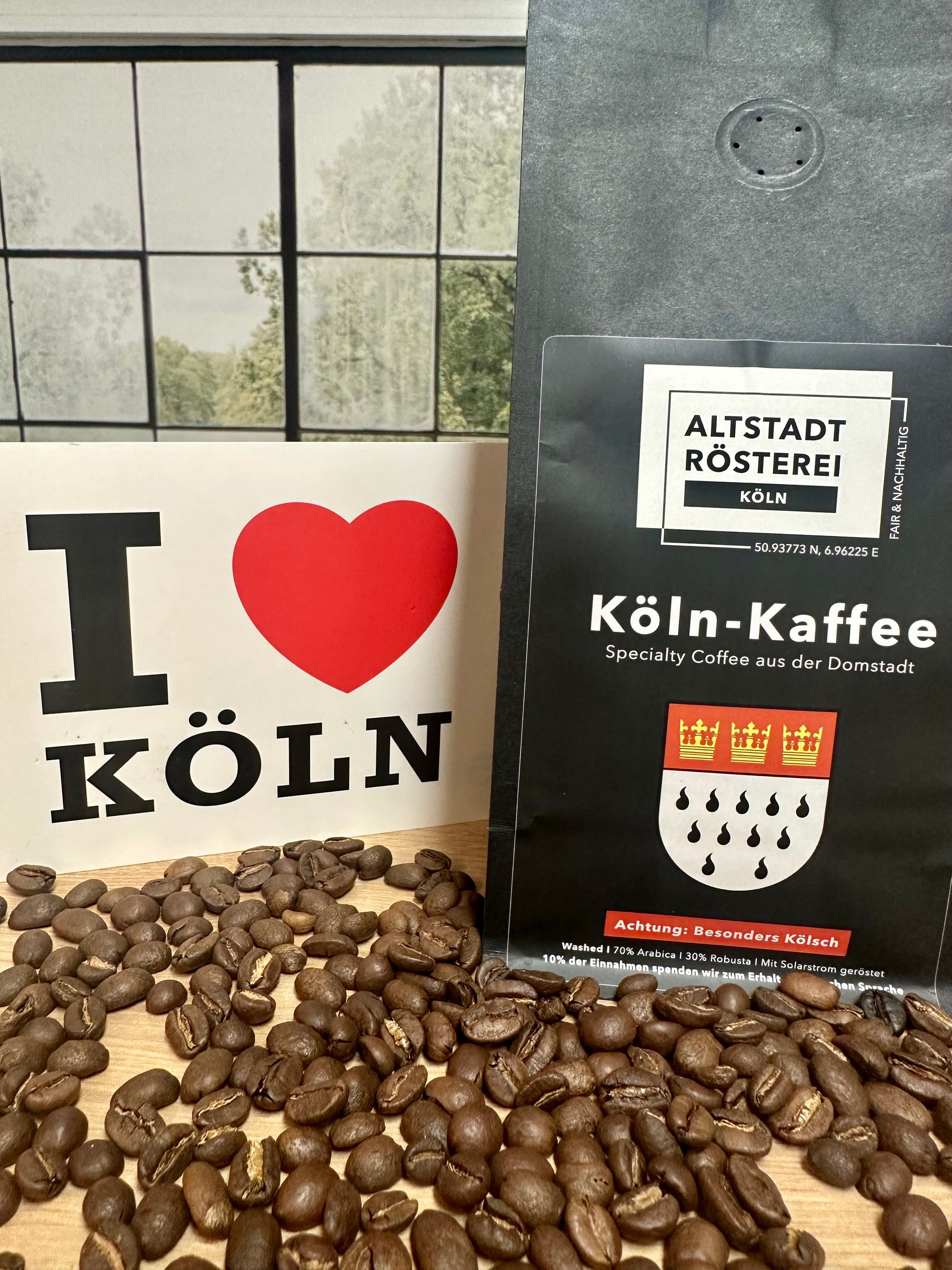  Eine Packung Köln-Kaffee von der Altstadt Rösterei Köln, umgeben von Kaffeebohnen. Daneben steht ein Schild mit der Aufschrift "I love Köln".