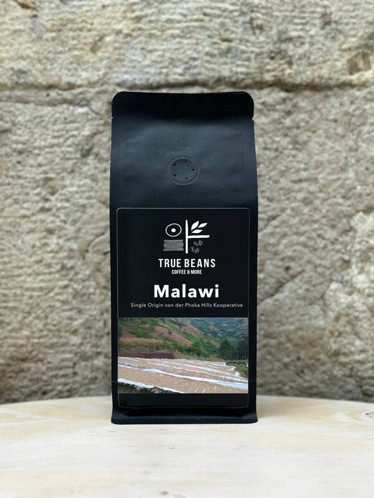 Ein Bild des Produkts Malawi 100% Arabica von True Beans auf einem Holztisch vor einer steinernen Säule.