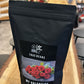 Eine Packung True Beans Kaffee "My Valentine" steht auf einem Holztisch. Die Verpackung zeigt ein Bild von roten Rosen und der Text auf der Packung beschreibt den Kaffee als Direct Trade, Social Impact und Organic. Im Hintergrund sind unscharf Blumentapeten und Regale zu sehen.