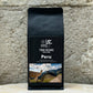 Ein Bild des Produkts Peru 100% Arabica von True Beans auf einem Holztisch vor einer steinernen Säule.