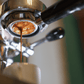 Nahaufnahme eines Espresso, der aus einer Espressomaschine in eine Tasse fließt, wobei der Kaffeefluss und die glänzenden Metallteile der Maschine im Fokus stehen.